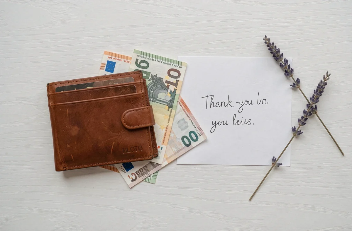 Billet en euros, portefeuille et carte manuscrite sur une table blanche symbolisant les étrennes pour la femme de ménage